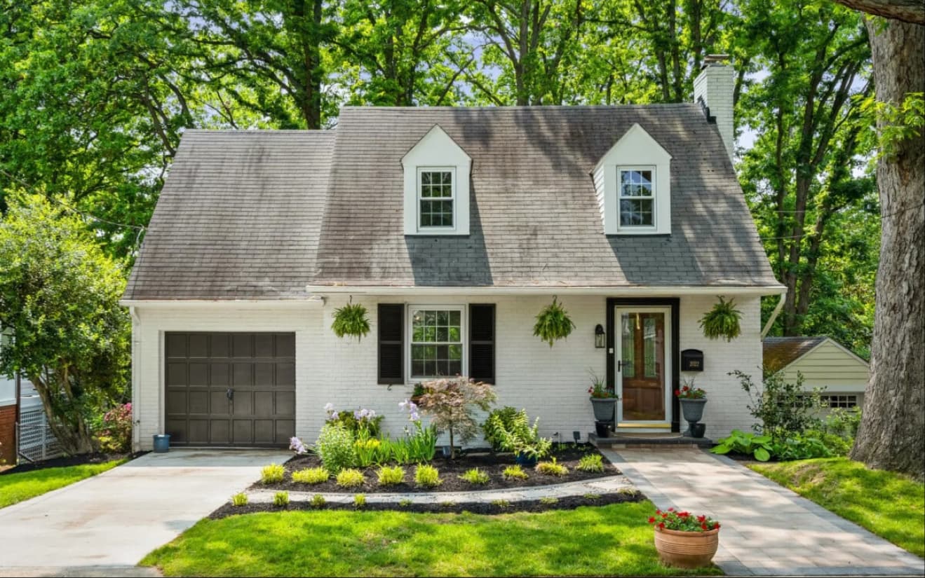 A charming white two-story house with a steep roof, black shutters, and a well-kept front yard